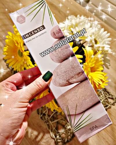 Caixa de incenso com pedras empilhadas e texto, segura com flores ao fundo