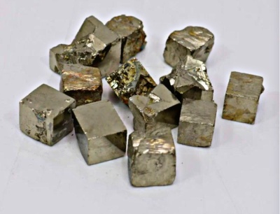 Peças cúbicas de mineral metálico dourado sobre superfície branca.