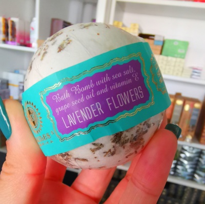 Bola efervescente de banho com flores de lavanda e etiqueta colorida segurada por mão