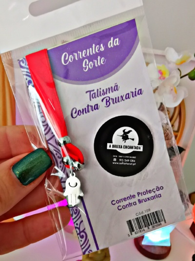 Talismã com fita vermelha e pendente em formato de mão em embalagem plástica, cartão com texto em português.