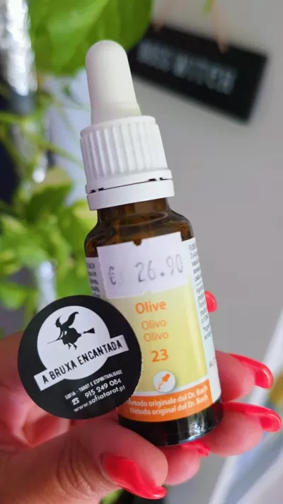 Frasco âmbar com conta-gotas branco e etiqueta amarela, segurado por mão com unhas vermelhas