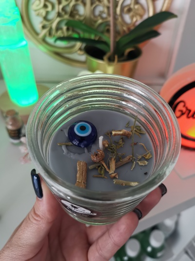 Vela cinzenta em frasco de vidro com olho turco azul e elementos secos na cera