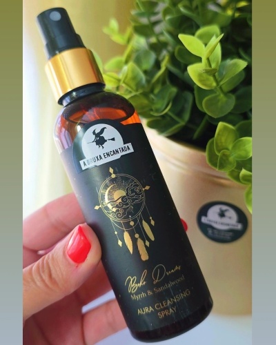 Frasco spray âmbar com etiqueta preta e dourada de limpeza de aura junto a planta verde num vaso bege