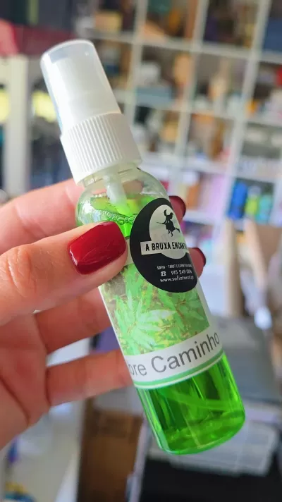 Frasco de spray com líquido verde e etiqueta preta e branca segurado por mão com unhas vermelhas