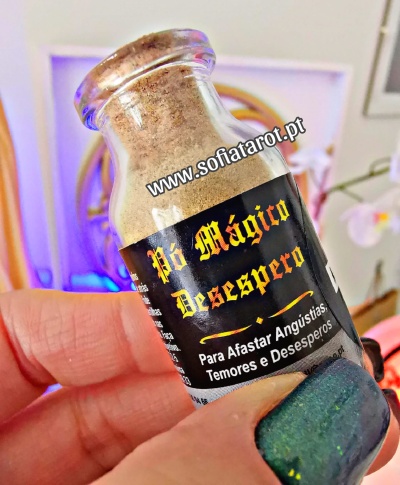 Frasco pequeno de vidro com pó, rótulo preto com texto dourado e branco, mão com unhas verdes segura o frasco