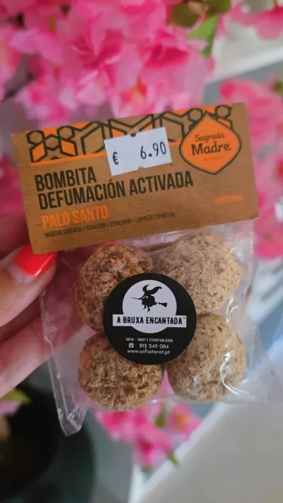 Pacote de bombitas de defumação activada Palo Santo com etiqueta castanha e flores cor-de-rosa ao fundo