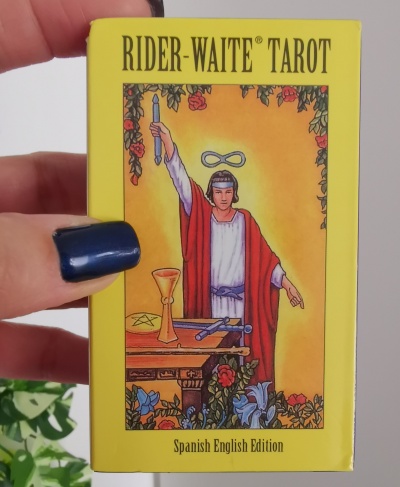 Caixa amarela de baralho Rider-Waite Tarot com figura de maestro de vestes vermelha e branca segurando uma vara.
