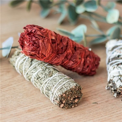 Três charutos de ervas na mesa, um vermelho e dois verdes amarrados, folhas ao fundo