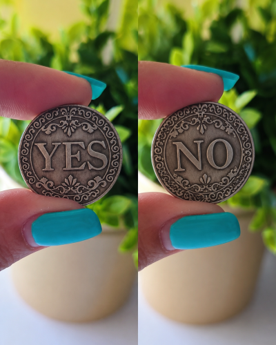 Moedas metálicas decorativas com YES e NO, seguradas por dedos com unhas azuis, fundo de planta verde