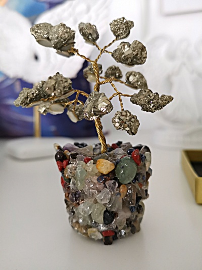 Árvore decorativa com folhas prateadas e vaso coberto de pedras coloridas