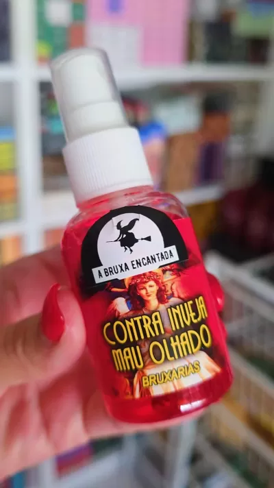 Frasco spray líquido vermelho com rótulo ilustrado e texto contra inveja mau olhado