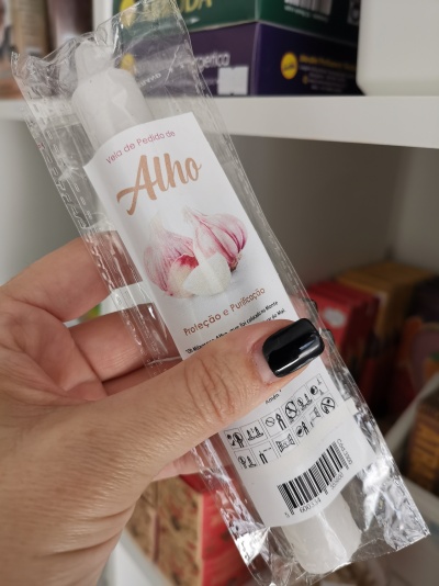 Vela branca de alho em embalagem plástica com etiqueta na mão diante de prateleira