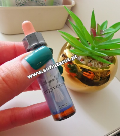 frasco de vidro com conta-gotas e rótulo azul segurado por mão com unhas verdes perto de planta suculenta