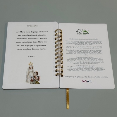 Livro encadernado em espiral aberto com texto em português e imagem religiosa no interior.