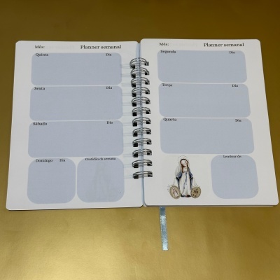 Planner semanal aberto com dias da semana em português e ilustração religiosa