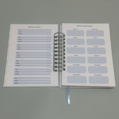 Agenda aberta com páginas para anotar senhas e datas importantes, em formato espiral e capa transparente.