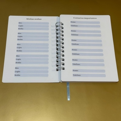 Caderno branco aberto com páginas para senhas e contactos, encadernação espiral, fita marcador azul