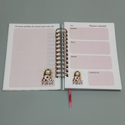 Caderno aberto com planner semanal e espaço para pedidos de oração, com figura feminina decorativa