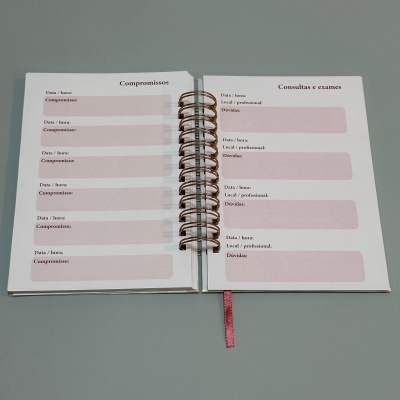 Caderno aberto com páginas para registo de compromissos e consultas, espiral metálica e marcador rosa