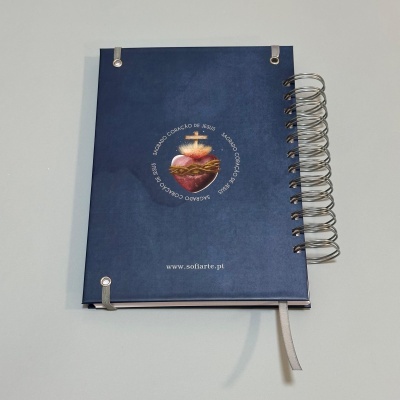Caderno capa azul com elástico e espiral, com coração e cruz na capa