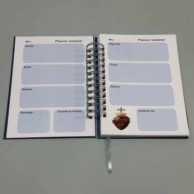 Agenda semanal aberta com blocos azuis claros e imagem religiosa.