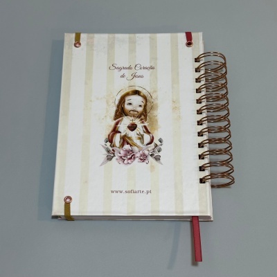 Caderno com capa decorada com imagem do Sagrado Coração de Jesus e texto, com espiral dourada