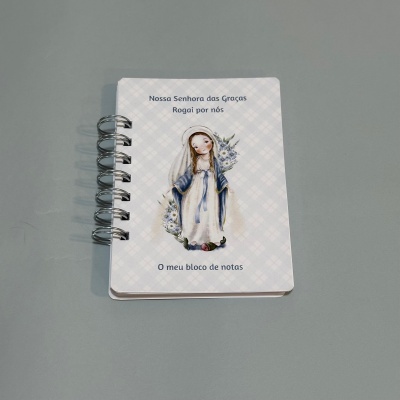 Bloco de notas com capa ilustrada de Nossa Senhora das Graças e texto em português
