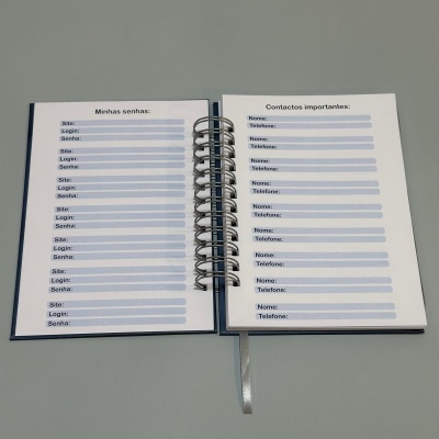 Caderno aberto com páginas para inscrições de senhas e contactos importantes, com encadernação espiral e fita cinza.