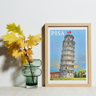 Vaso verde com folhas amarelas ao lado de quadro da Torre de Pisa com moldura de madeira
