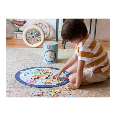 Criança a montar puzzle circular do mapa-múndi com lata azul ao lado.