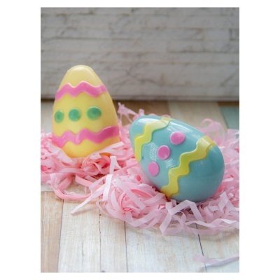 Dois ovos decorativos coloridos sobre tiras de papel rosa e fundo de madeira clara.