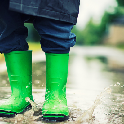 Botas de borracha verdes em estrada molhada com água a espirrar