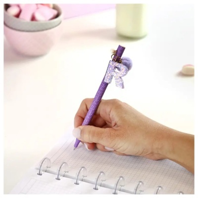 Mão segurando caneta roxa com adereço da letra R sobre caderno quadriculado