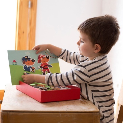 Criança a brincar com brinquedo educativo de figuras de cães em uniforme numa caixa vermelha