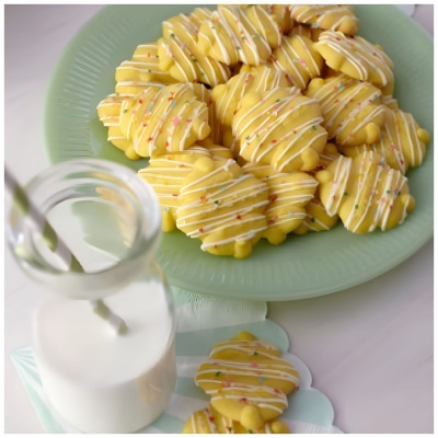 Bolachas amarelas decoradas numa placa verde com garrafa de leite e palha