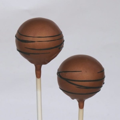 Dois cake pops redondos com cobertura castanha e linhas pretas em palitos brancos