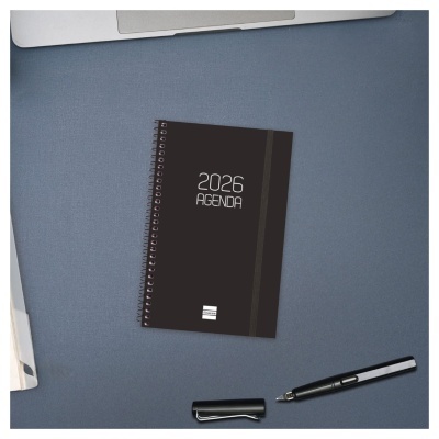 Agenda preta 2026 com espiral e elástico sobre mesa azul