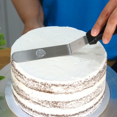 Espátula com gravação a espalhar cobertura num bolo branco de camadas