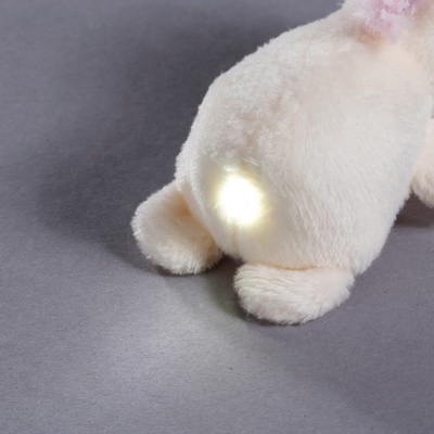 Brinquedo de pelúcia branco com luz LED na parte traseira sobre superfície cinzenta