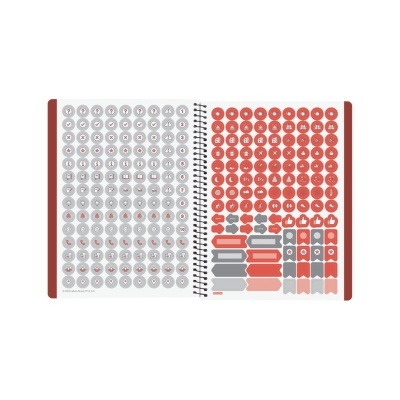 Caderno aberto com autocolantes vermelhos e cinzentos com símbolos e letras.