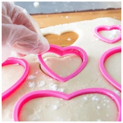 Conjunto de cortadores de biscoitos rosa em forma de coração a cortar massa branca.