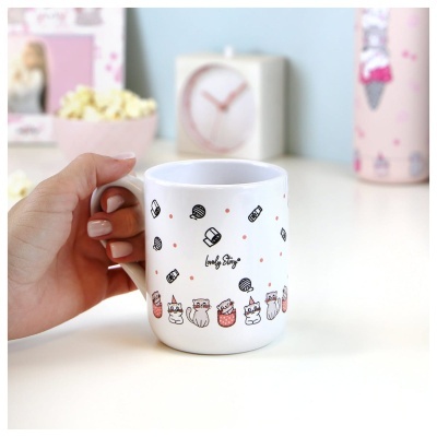 Caneca branca com desenhos de gatos e texto lovely Story sendo segurada por uma mão