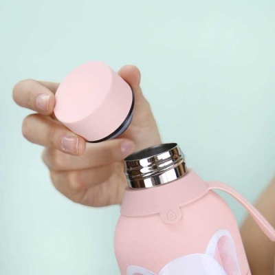 Mão a segurar a tampa de uma garrafa térmica rosa com parte metálica