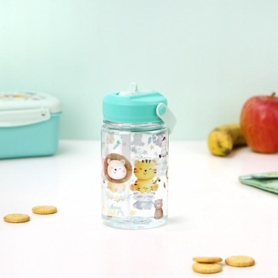 Garrafa transparente com tampa azul e desenhos de animais numa mesa branca com bolachas e fruta
