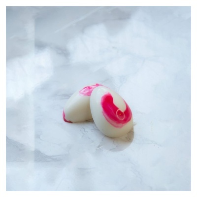 Dois sabonetes ovais brancos com manchas cor-de-rosa em superfície marmoreada