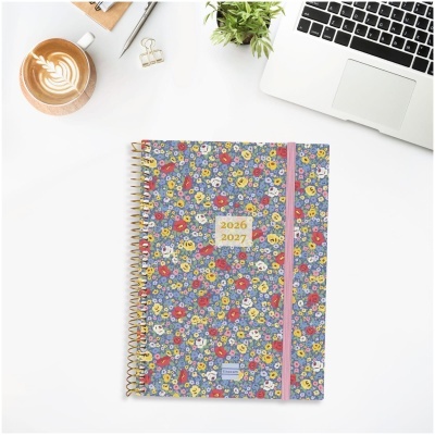 Agenda floral 2026-2027 com elástico rosa sobre mesa branca com laptop e café