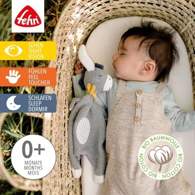 Bebé a dormir com brinquedo de peluche cinzento numa cama de verga, com etiquetas e selo de algodão biológico