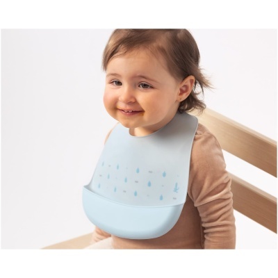 Bebé a usar babete azul claro com padrão de gotas sentado numa cadeira de madeira clara