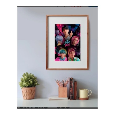 Poster colorido emoldurado com personagens de animação e texto SAINT BOYS na parede cinza acima da secretária