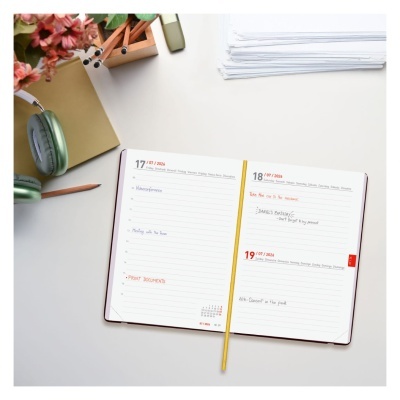 Agenda semanal aberta com datas legíveis e texto manuscrito, com fundo de mesa branca e material de escritório próximo